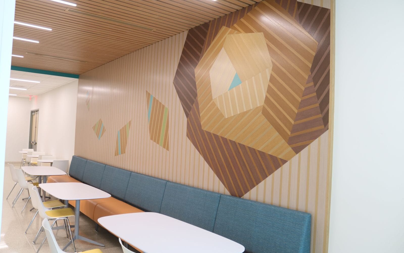 Abstract geometric mural on a wall above blue seating and white tables in a modern indoor space.