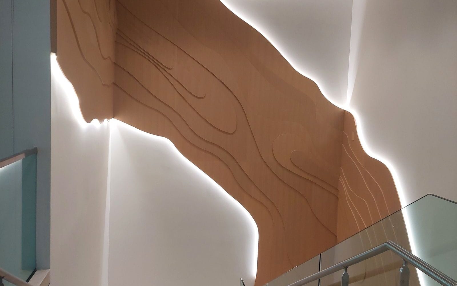Modern interior with wooden wall feature, illuminated edges, and sleek glass railings leading down a staircase.