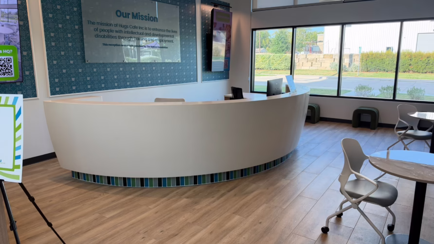 Modern reception area with a curved desk, chairs, tables, and a large mission statement on the wall.