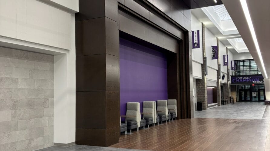 Modern hallway with high ceilings, seating area, and a mix of wooden and tiled flooring, featuring purple accent wall.