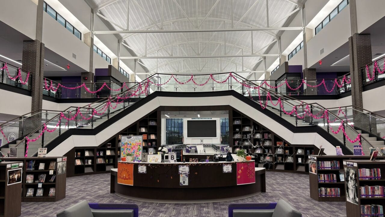 Modern library interior with central staircase, bookshelves, and seating area under high ceiling.