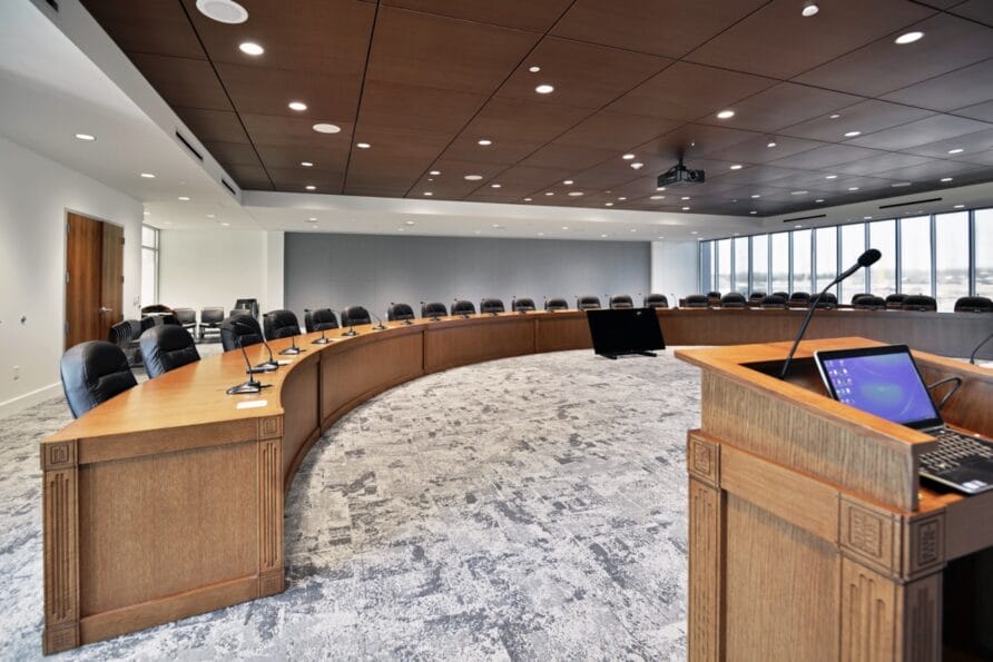 Modern conference room with a large wooden table, leather chairs, and a projector screen.
