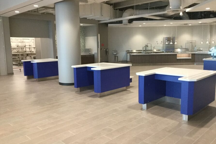 Modern office space with blue and white desks, light wood flooring, and exposed ceiling ducts.