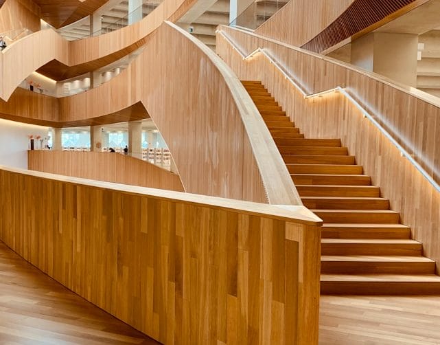 Curved wood reception desk beside an open staircase in a building lobby